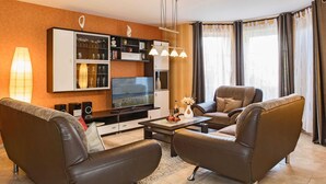 Moderni olohuone, jossa on nahkasohvat, litteänäyttöinen televisio, lasiovilla varustettu kaappi ja ruokapöytä.
