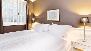 Et hotelværelse med en stor seng, et sengebord, en lampe og et vindue med gardiner.