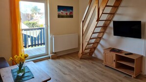 A room with a wooden staircase, a radiator, a TV mounted on the wall, and a window with curtains. - OR - Ferienhaus Mönchgutperle (Middelhagen)