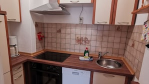 A compact kitchen with wooden cabinets, a built-in oven, a dishwasher, and a sink. - OR - Ferienhaus Mönchgutperle (Middelhagen)