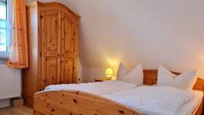 A wooden bed with white bedding, a nightstand with a lamp, and a large wooden wardrobe. - OR - Ferienhaus Mönchgutperle (Middelhagen)