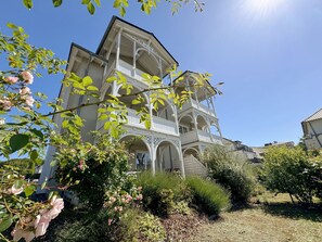A multi-story building with a balcony and a garden in front.