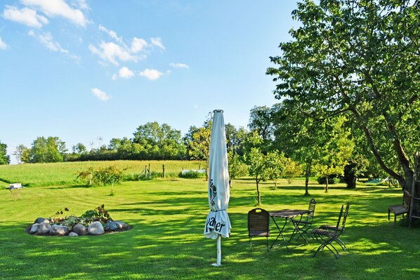 An outdoor seating area with a table and chairs, a white umbrella, and a grassy field in the background.