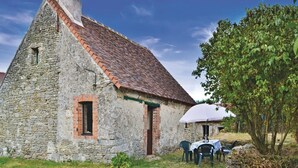 Ein Steinhaus mit Ziegeldach, einem kleinen Fenster und einer Tür. Vor der Tür stehen ein Tisch und Stühle unter einem weißen Sonnenschirm.