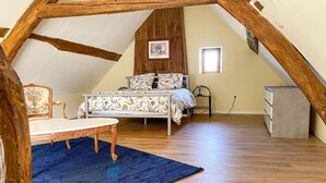 Ein gemütliches Schlafzimmer im Dachgeschoss mit Holzbalkendecke, einem Bett mit floralem Bettzeug, einem kleinen Tisch und einem Stuhl.