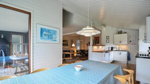 Una cocina moderna con armarios blancos, una zona de comedor con mantel azul y una lámpara colgante.