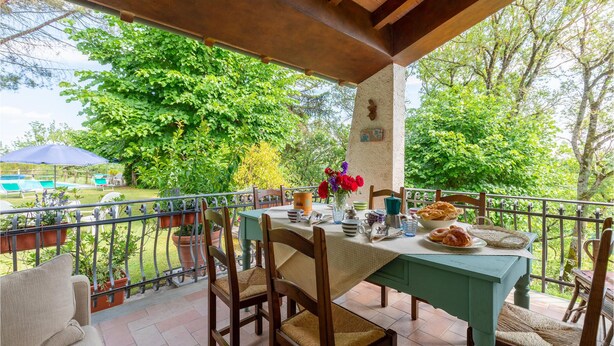 Eine überdachte Terrasse mit Esstisch, umgeben von Stühlen, mit Blick auf einen Swimmingpool und üppiges Grün.
