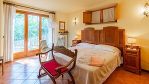 Ein Schlafzimmer mit einem großen Bett, einem hölzernen Stuhl mit rotem Kissen, einem Nachttisch aus Holz, einem an der Wand montierten Schrank und einem Fenster mit Vorhängen.