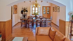 A cozy living room with a leather sofa, wooden dining table, and chairs. There is a chandelier, a wooden cabinet, and a world map on the wall. - Nice home in Pòrtol with kitchen (Pòrtol)