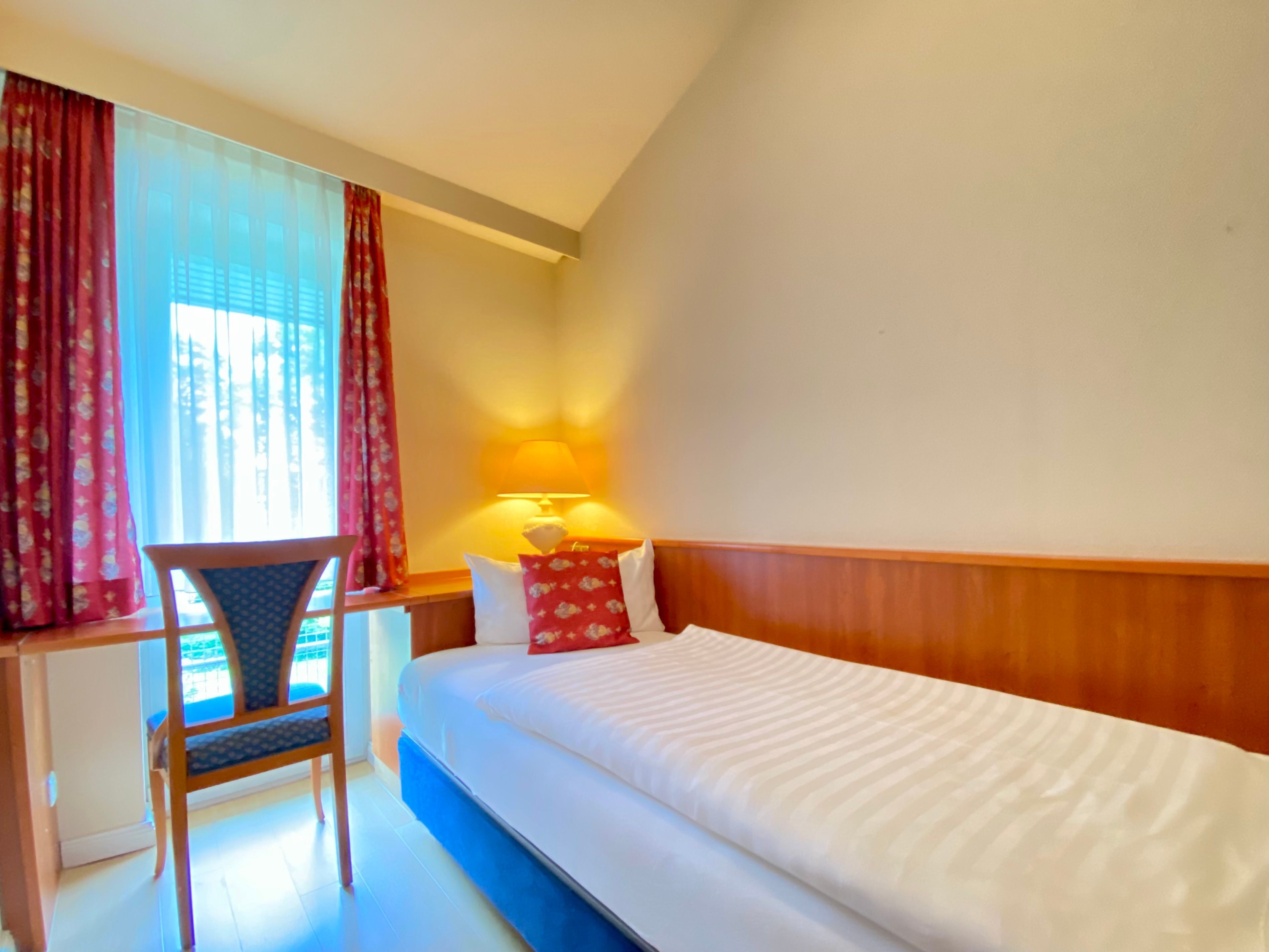 Une chambre d’hôtel avec un lit, un bureau, une chaise et une lampe.