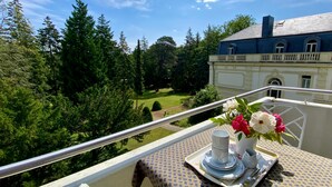 A balcony with a table set for tea, overlooking a lush garden and a classical building. - Residence Bleichröder App. Cosima, VS Sass (Heringsdorf)