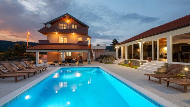 Une maison à deux étages avec une piscine, un espace extérieur aménagé pour s’asseoir et une terrasse bien éclairée.