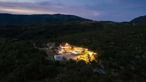 Un grand immeuble à étages, doté d’une façade bien éclairée, entouré d’une forêt dense et de collines.