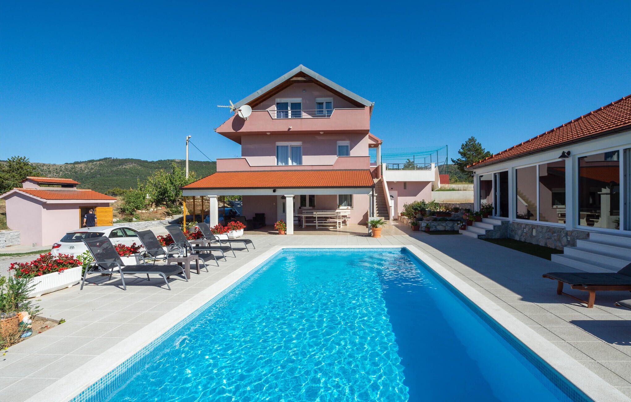 A two-story building with a swimming pool, outdoor seating, and a view of the hills.