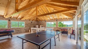 Un grand espace intérieur aménagé avec une table de ping-pong, un baby-foot et une table de billard. De grandes fenêtres offrent une vue sur l’extérieur.