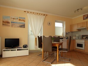 A compact kitchen with a dining area, featuring a TV, cabinets, and a clock on the wall. - Waldstr. Wa30-03 - Wa30-03 (Kühlungsborn)