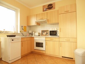 A compact kitchen with wooden cabinets, a dishwasher, a stove, and a microwave.