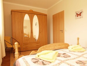 A bedroom with a wooden wardrobe, a bed with a patterned bedspread, and a chair.