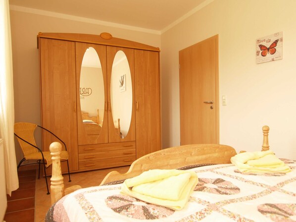 A bedroom with a wooden wardrobe, a bed with a patterned bedspread, and a chair.