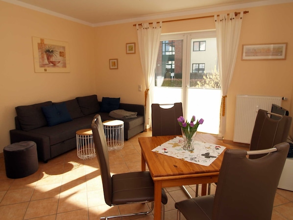 A living room with a sofa, two chairs, a table with a vase of flowers, and a window with curtains.