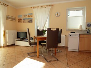 A compact kitchen with a dining table, chairs, a TV, a refrigerator, and a window with blinds.