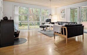 A spacious living room with a large window, a black leather sofa, a wooden coffee table, and a black grill. - Gorgeous home in Nexø with WiFi (Nexø)