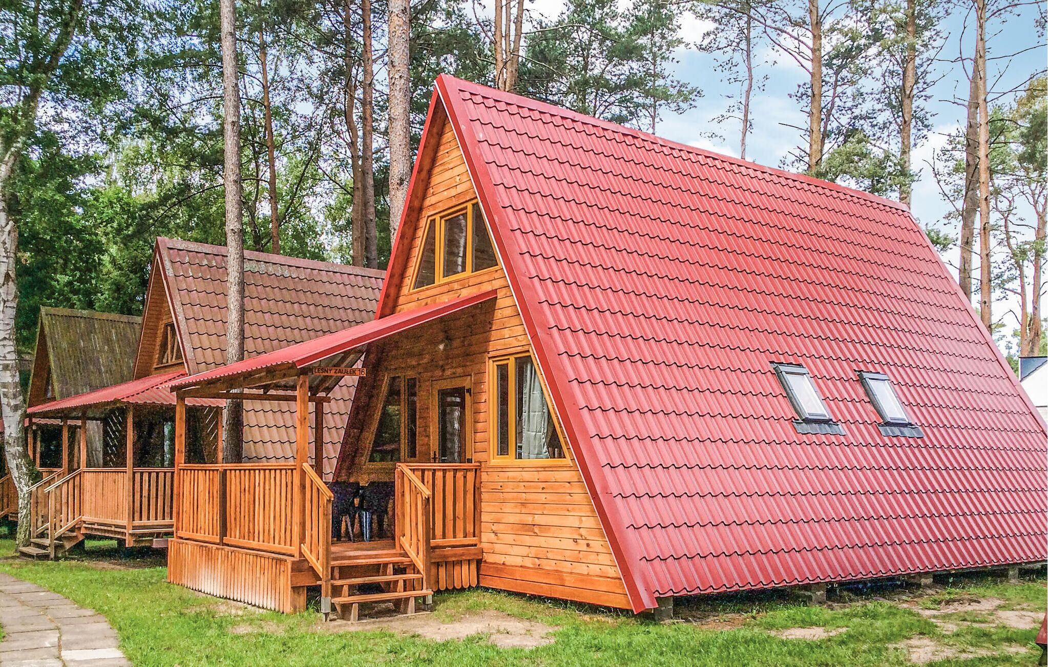 Una cabaña de madera con techo rojo, un porche y un ventanal visible.