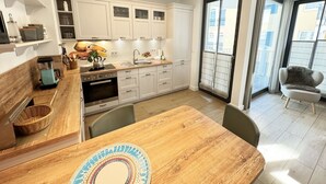 Eine moderne Küche mit weißen Schränken, einem Holztisch und Blick ins Freie durch große Fenster.