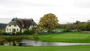 Una casa con un estanque delantero, un campo de golf y un gran árbol.