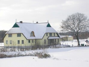 Een groot, twee verdiepingen tellend huis met een steil dak, veel ramen en een besneeerd landschap.