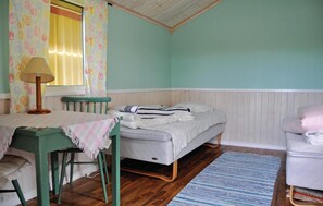 Ein Zimmer mit einem Bett, einem Tisch mit Lampe, einem Sessel und einem Fenster mit Vorhängen.
