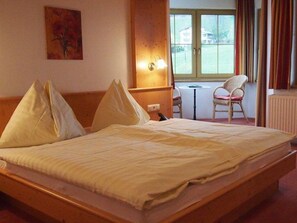A hotel room with a bed, a chair, a table, and a window with curtains. - 104 - Pension Stallinger (Weyregg am Attersee)