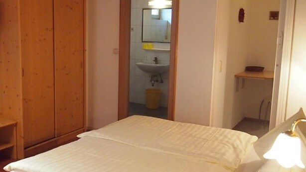 Un dormitorio con cama, armario de madera y baño visible a través de una puerta abierta.