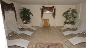 Una habitación con cuatro sillones reclinables, una silla de madera en el centro y dos macetas con plantas.