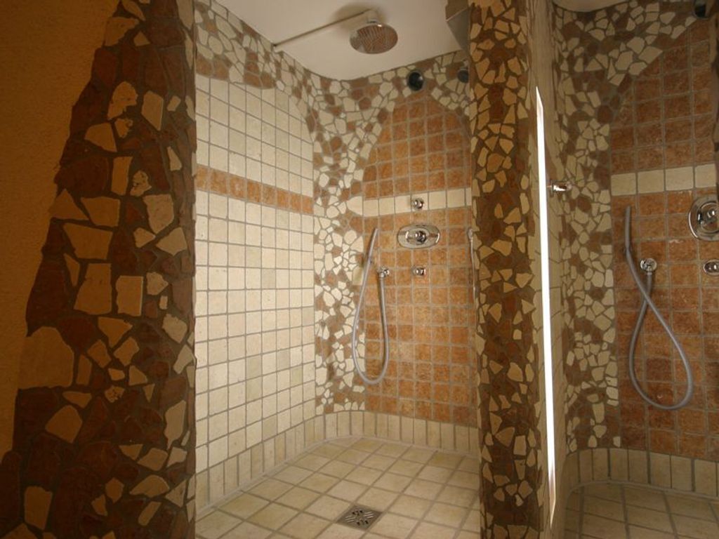 Una doccia con pareti in mosaico e uno scarico al centro.