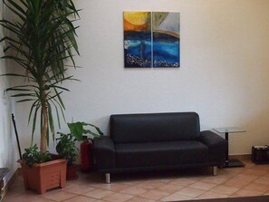 Een kamer met een zwarte bank, een potplant en een schilderij aan de muur.