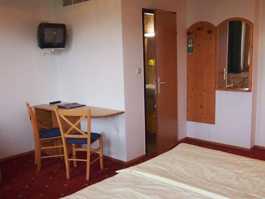 Una habitación con una cama, un escritorio con una silla, un televisor fijado a la pared y una puerta con un espejo.