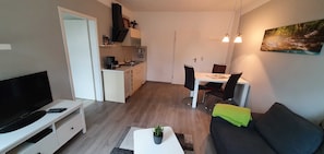 Un espace de vie compact comprenant un téléviseur, un canapé, une table à manger, des chaises et un coin cuisine.