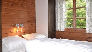 Un dormitorio con paneles de madera, una cama con ropa blanca, dos lámparas fijadas a la pared y un ventanal con cortinas estampadas.