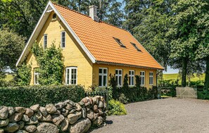 A yellow house with a red-tiled roof, a stone wall in front, and a gravel driveway. - Stunning apartment in Aakirkeby (Aakirkeby)