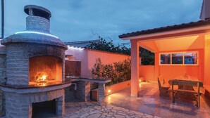 Un horno de piedra al aire libre con fuego, una mesa de comedor con sillas y un porche cubierto.