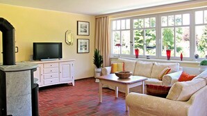 A living room with a fireplace, a television, a sofa, and a window with a view of greenery. - Holiday Sundevit 1st - Holiday Sundevit (Prerow)