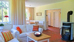 A cozy living room with a white sofa, a wooden table with a bowl, and a black wood stove. - Holiday Sundevit 1st - Holiday Sundevit (Prerow)