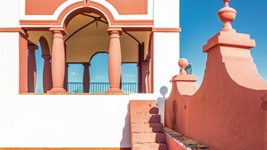 Un bâtiment doté d’un toit recouvert de tuiles rouges, d’un balcon avec une balustrade et d’un escalier menant à l’entrée.