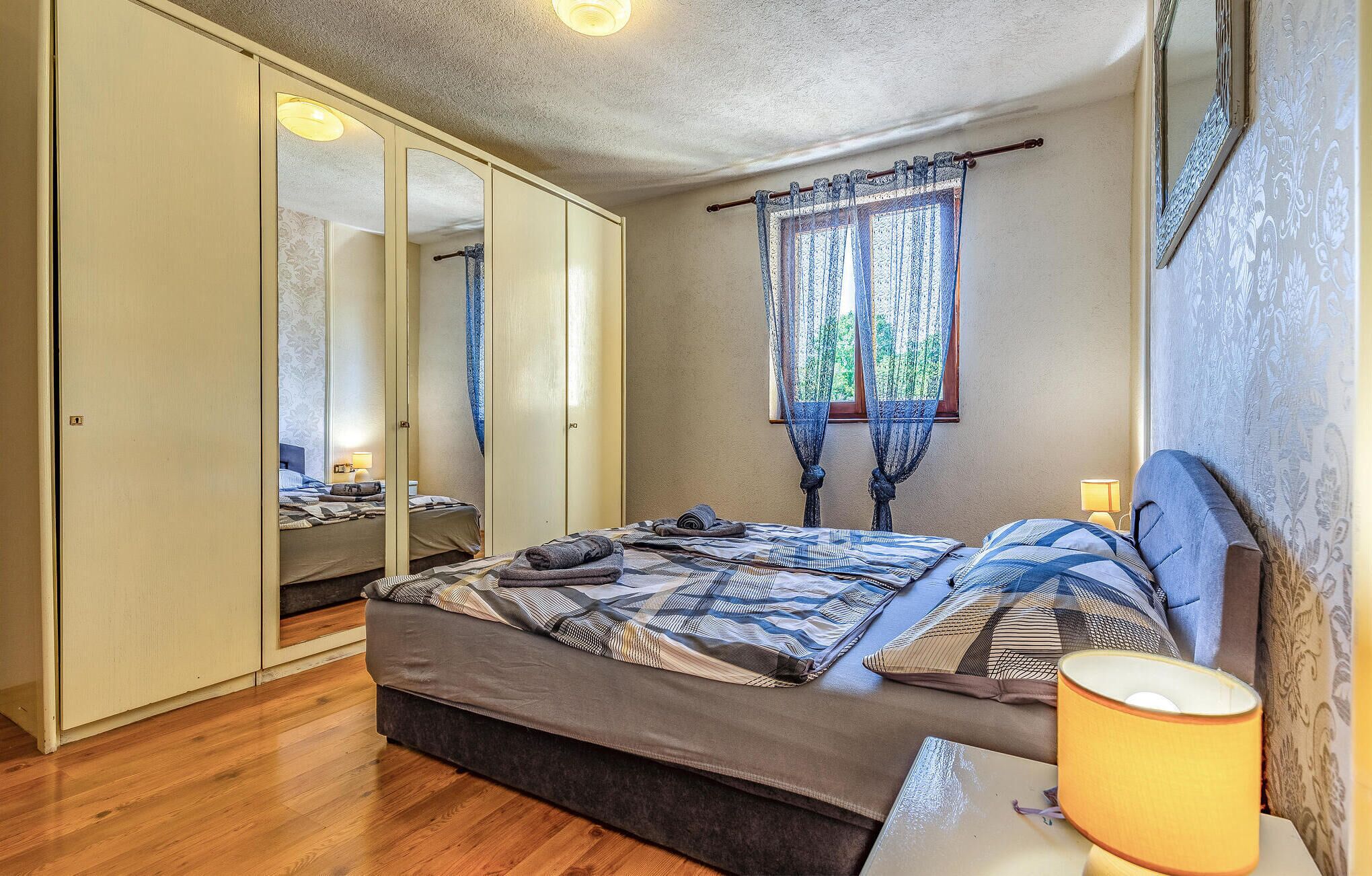 Un dormitorio con cama, mesitas de noche, armario y ventana con cortinas.