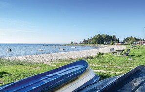 Una playa con barcos, una orilla arenosa y una zona de césped con bancos.