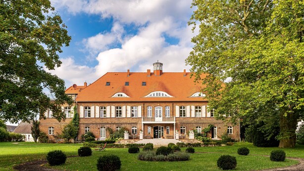 Ein großes Backsteingebäude mit einer symmetrischen Fassade, zahlreichen Fenstern und einem zentralen Eingang.