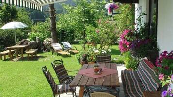 Eine Terrasse im Freien mit einem Holztisch und Stühlen, umgeben von üppigem Grün und blühenden Pflanzen.