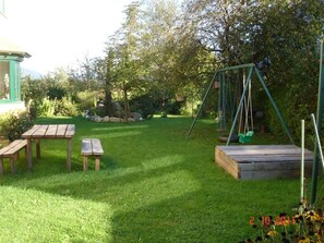 A backyard with a swing set, picnic tables, and a wooden deck.
