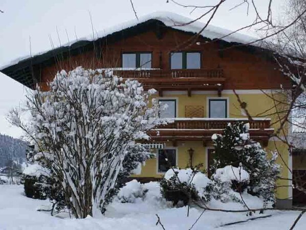 A two-story building with a balcony, surrounded by snow-covered trees.